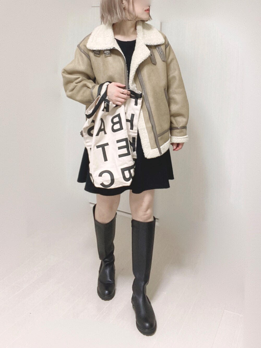 ブラック系のブーツ、ベージュ系のムートンコート、ホワイト系のトートバッグを着用したレディースの秋コーディネートの5枚目の写真