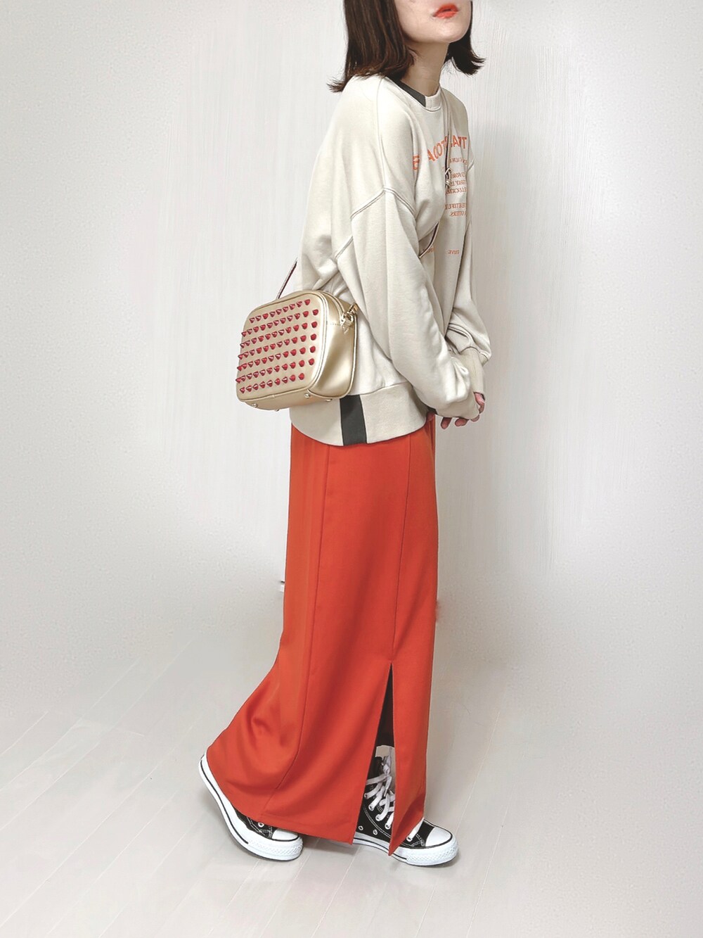 ベージュ系のスウェット、ゴールド系のショルダーバッグ、オレンジ系のスカートを着用したレディースの春コーディネートの4枚目の写真