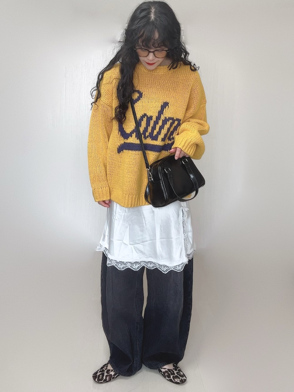 イエロー系のニット/セーター、ブラック系のデニムパンツ、ホワイト系のワンピースを着用したレディースの春コーディネートの2枚目の写真