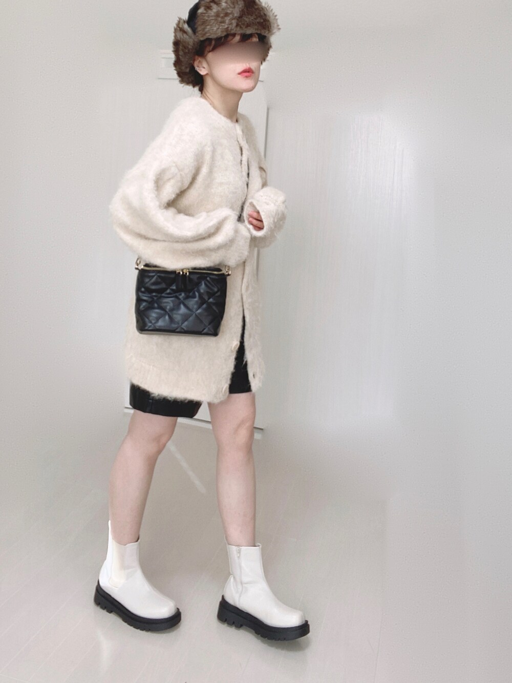 ホワイト系のブーツ、ベージュ系のカーディガン/ボレロ、ブラック系のショルダーバッグを着用したレディースの冬コーディネートの4枚目の写真