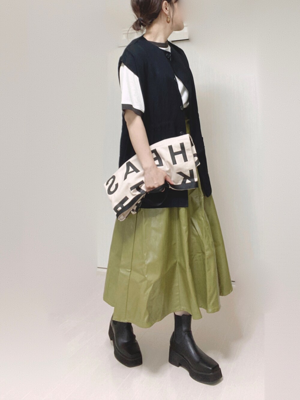 ブラック系のベスト、ホワイト系のトートバッグ、グリーン系のスカートを着用したレディースの秋コーディネートの5枚目の写真