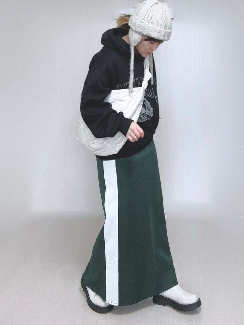 ブラック系のパーカー、ホワイト系のショルダーバッグ、グリーン系のスカートを着用したレディースの冬コーディネートの2枚目の写真