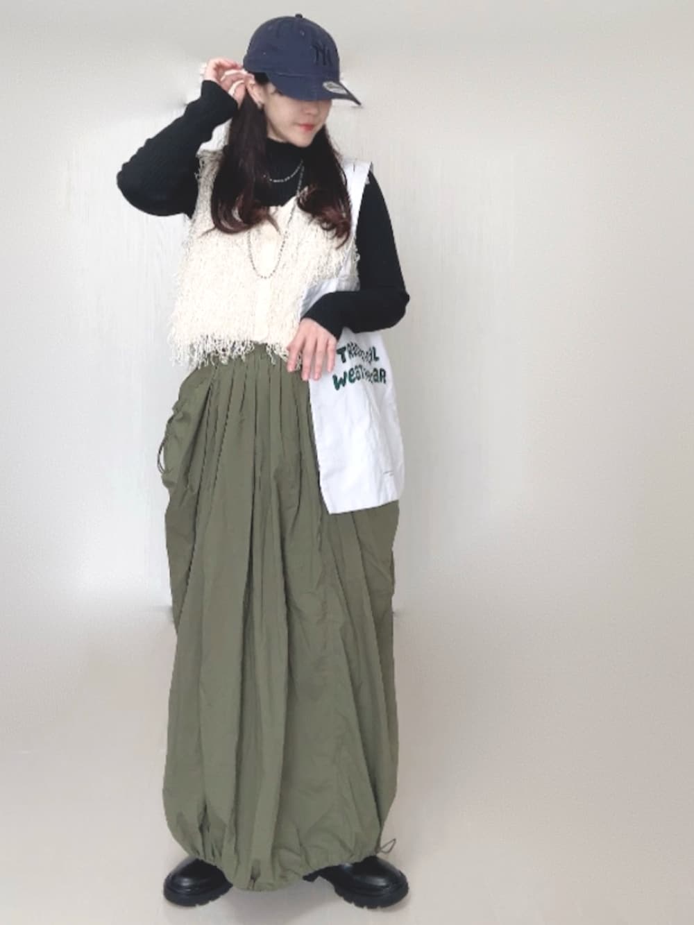 ホワイト系のベスト、ブラック系のニット/セーター、グリーン系のスカートを着用したレディースの秋コーディネートの2枚目の写真