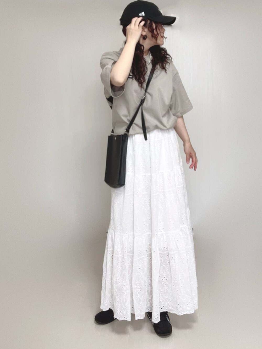 ブラック系のショルダーバッグ、ベージュ系のTシャツ/カットソー、ホワイト系のスカートを着用したレディースの夏コーディネートの2枚目の写真