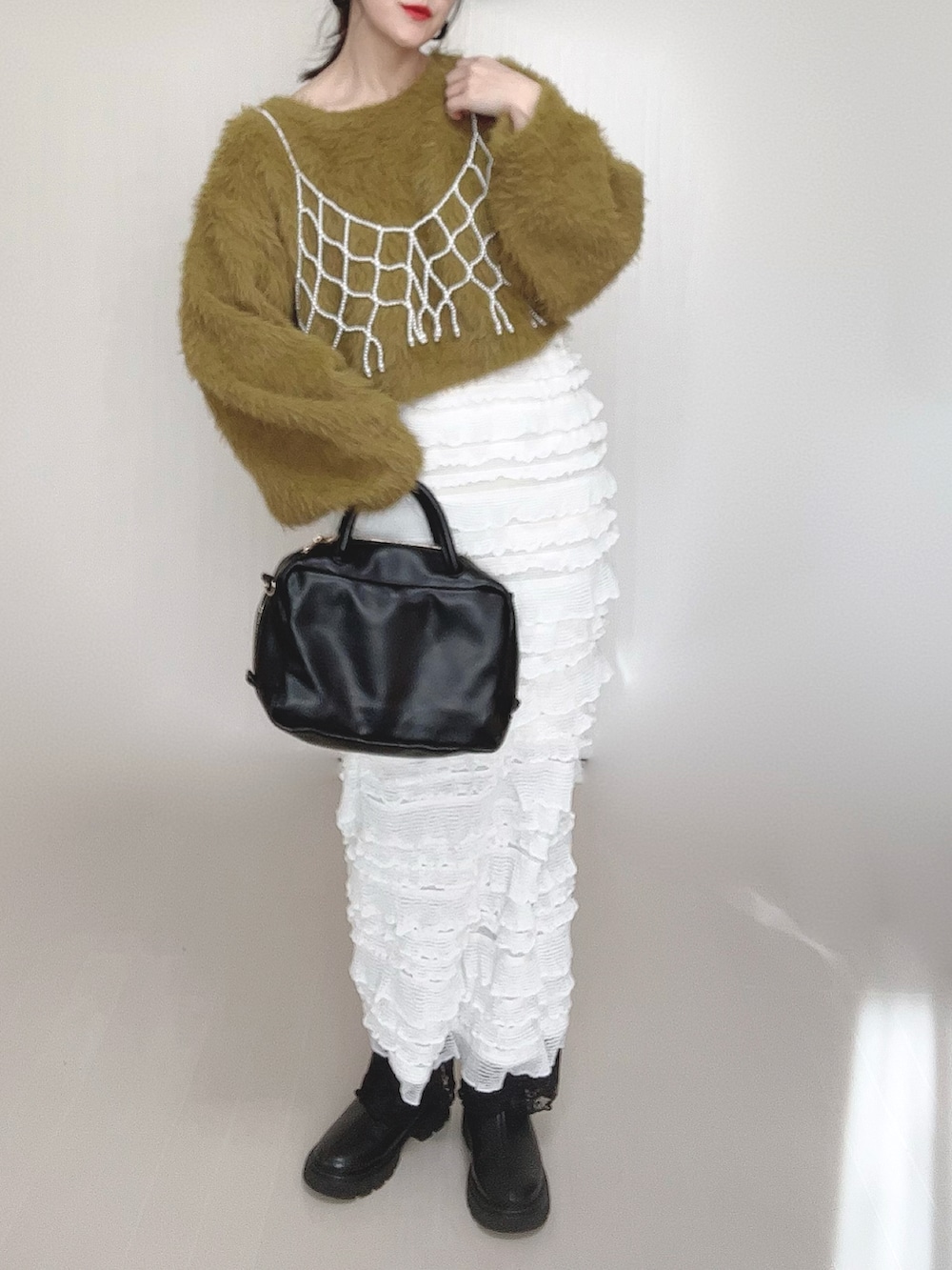 グリーン系のニット/セーター、ホワイト系のベスト、ブラック系のボストンバッグを着用したレディースの冬コーディネートの3枚目の写真