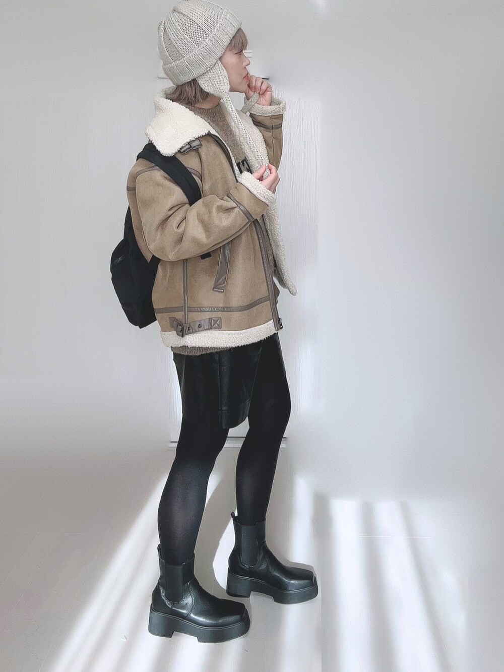 ベージュ系のムートンコート、ベージュ系のニット/セーター、ブラック系のバックパック/リュックを着用したレディースの冬コーディネートの2枚目の写真