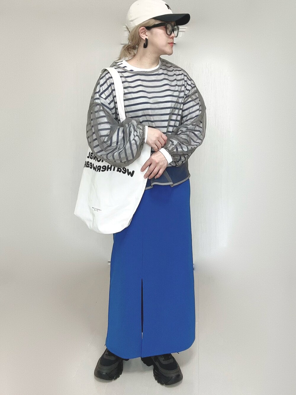 ブルー系のスカート、ホワイト系のトートバッグ、ブラック系のスニーカーを着用したレディースの春コーディネートの4枚目の写真