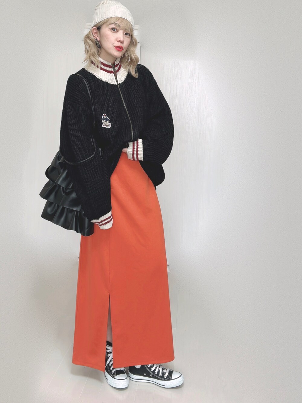 ブラック系のニット/セーター、オレンジ系のスカート、ブラック系のスニーカーを着用したレディースの秋コーディネートの3枚目の写真