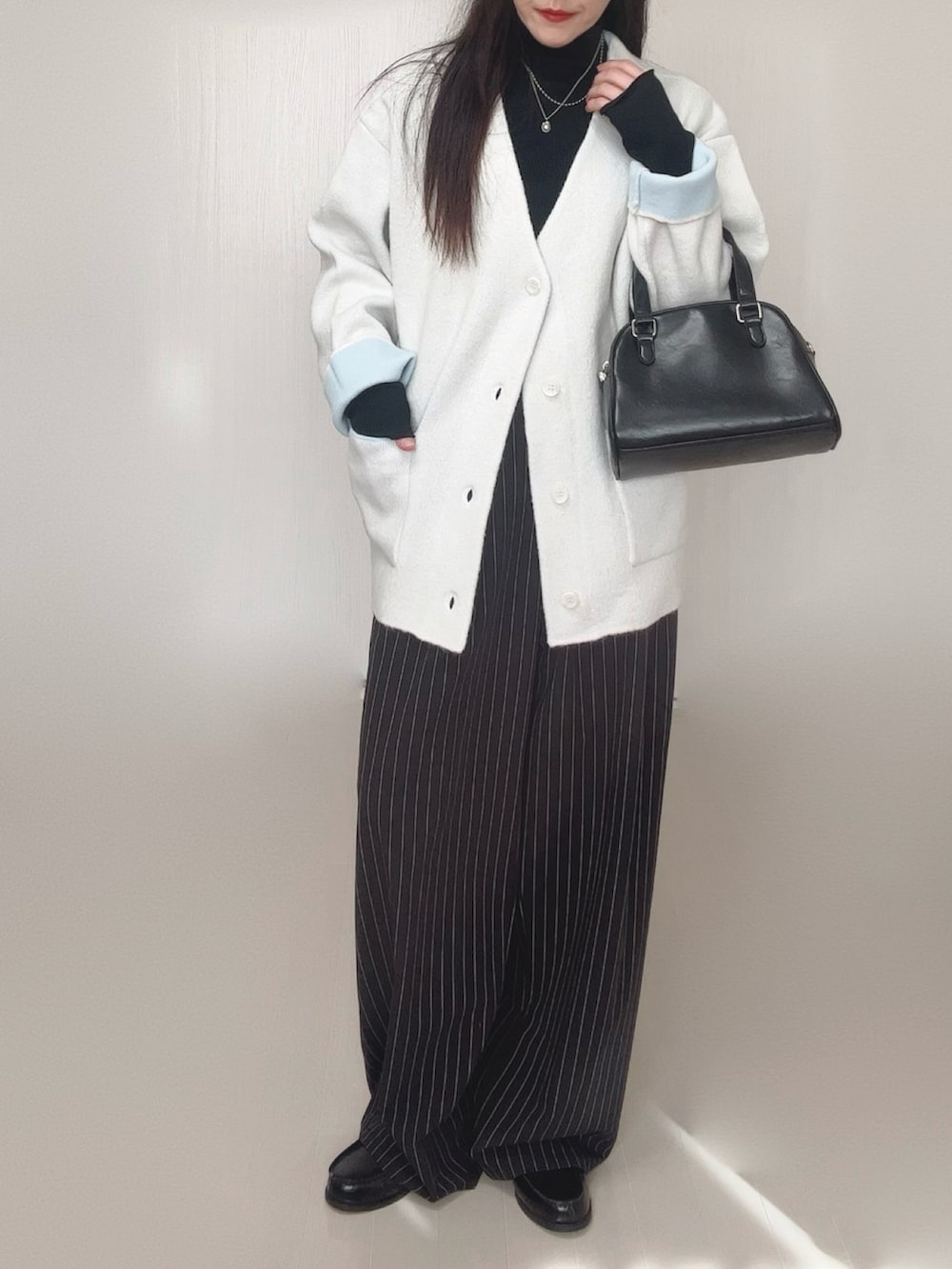 ホワイト系のカーディガン/ボレロ、ブラック系のTシャツ/カットソー、ブラック系のスラックスを着用したレディースの冬コーディネートの5枚目の写真