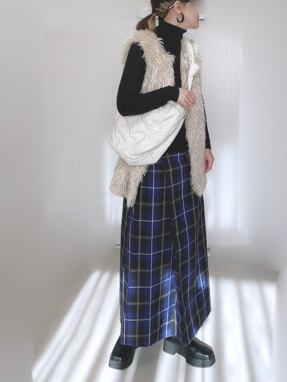 ホワイト系のベスト、ホワイト系のショルダーバッグ、ブラック系のブーツを着用したレディースの冬コーディネートの5枚目の写真