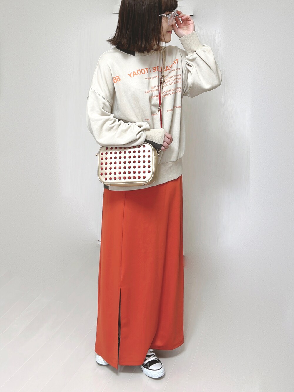 ベージュ系のスウェット、ゴールド系のショルダーバッグ、オレンジ系のスカートを着用したレディースの春コーディネートの3枚目の写真