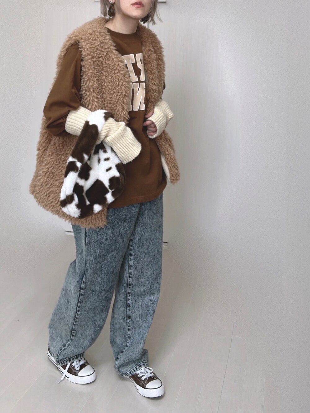 イエロー系のベスト、ブラウン系のTシャツ/カットソー、ブルー系のデニムパンツを着用したレディースの春コーディネートの2枚目の写真