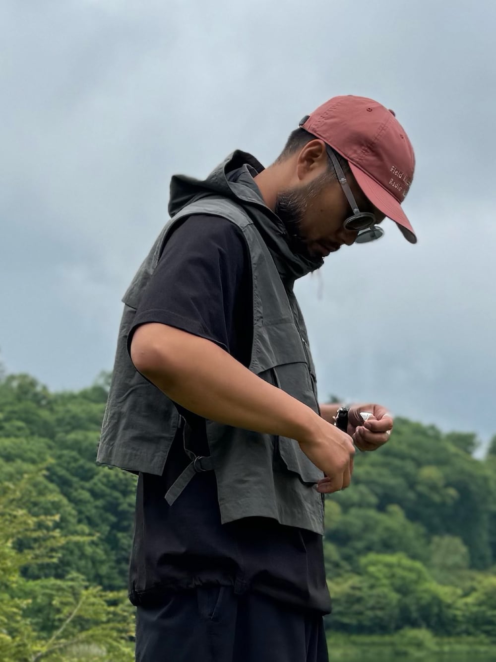 ブラック系のTシャツ/カットソー、グレー系のダウンベスト、ブラック系のメガネを着用したメンズの夏コーディネートの2枚目の写真
