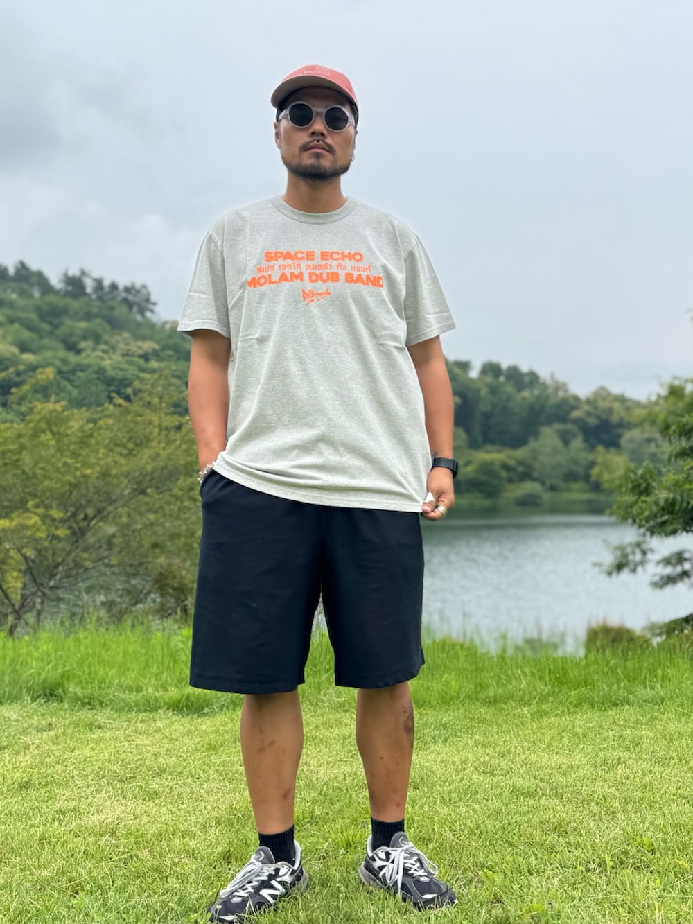 グレー系のTシャツ/カットソー、ブラック系のメガネ、オレンジ系のキャップを着用したメンズの夏コーディネートの3枚目の写真