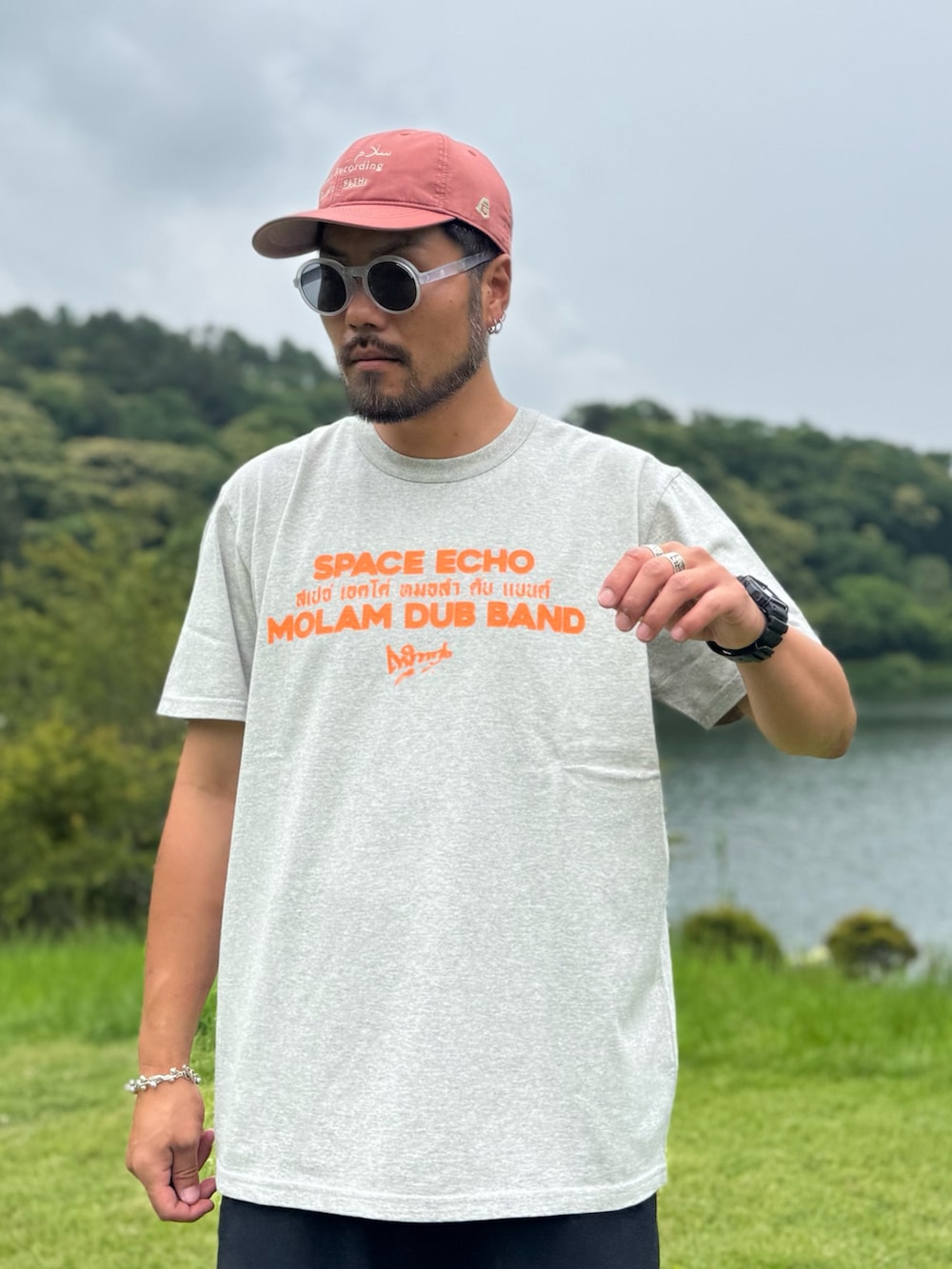 グレー系のTシャツ/カットソー、ブラック系のメガネ、オレンジ系のキャップを着用したメンズの夏コーディネートの2枚目の写真