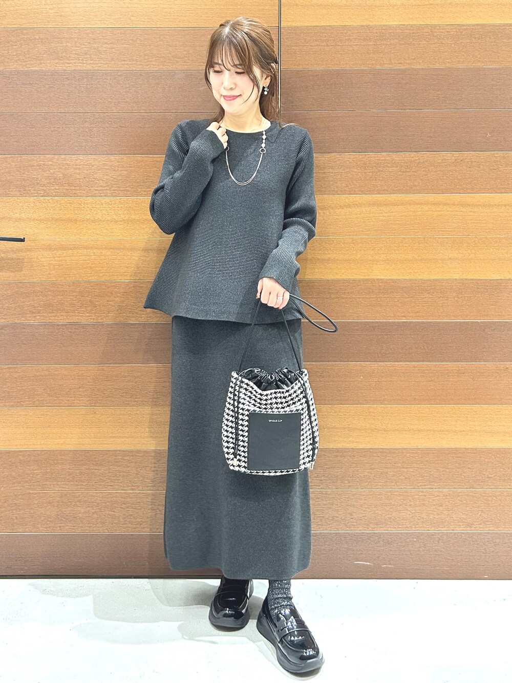グレー系のニット/セーター、グレー系のスカート、ブラック系のショルダーバッグを着用したレディースの秋コーディネートの2枚目の写真