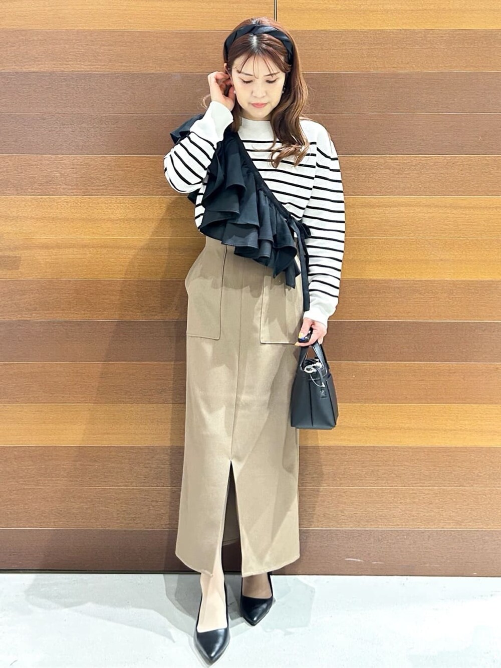 ブラック系のパンプス、ベージュ系のショルダーバッグ、ブラウン系のスカートを着用したレディースの春コーディネートの3枚目の写真