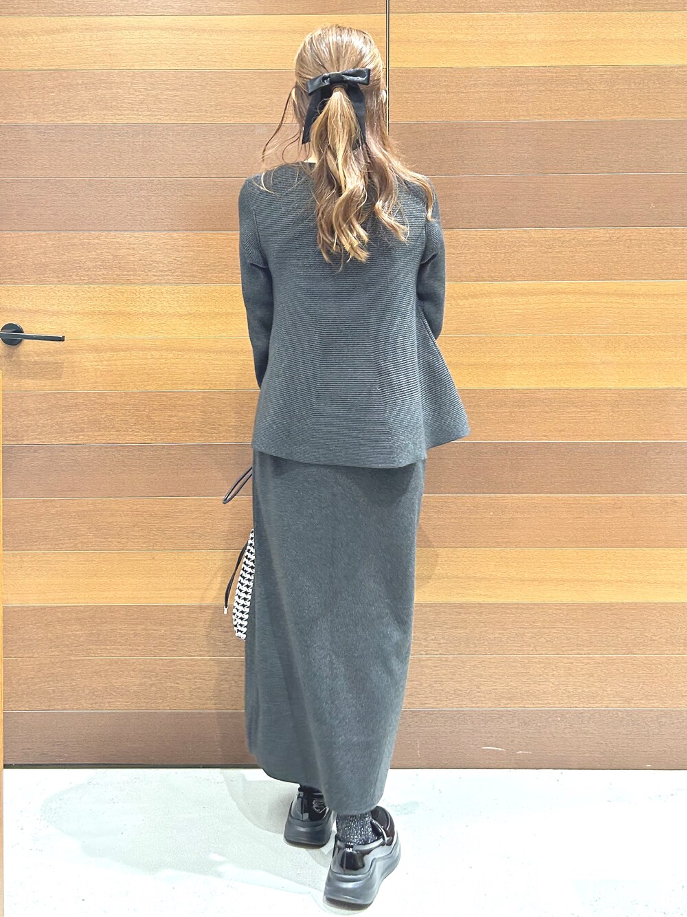 グレー系のニット/セーター、グレー系のスカート、ブラック系のショルダーバッグを着用したレディースの秋コーディネートの7枚目の写真