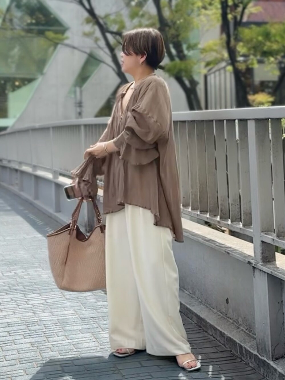 ブラウン系のシャツ/ブラウス、ホワイト系のスラックス、ブラウン系のトートバッグを着用したレディースの春コーディネートの2枚目の写真