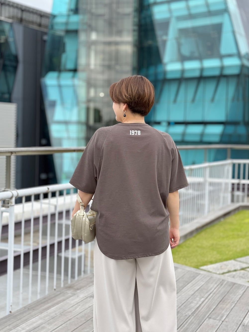 ブラウン系のTシャツ/カットソー、グレー系のスラックス、ゴールド系のショルダーバッグを着用したレディースの夏コーディネートの3枚目の写真