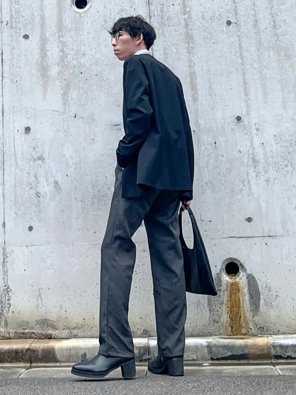 ブラック系のノーカラーコート、グレー系のスラックス、ブラック系のブーツを着用したメンズの春コーディネートの2枚目の写真