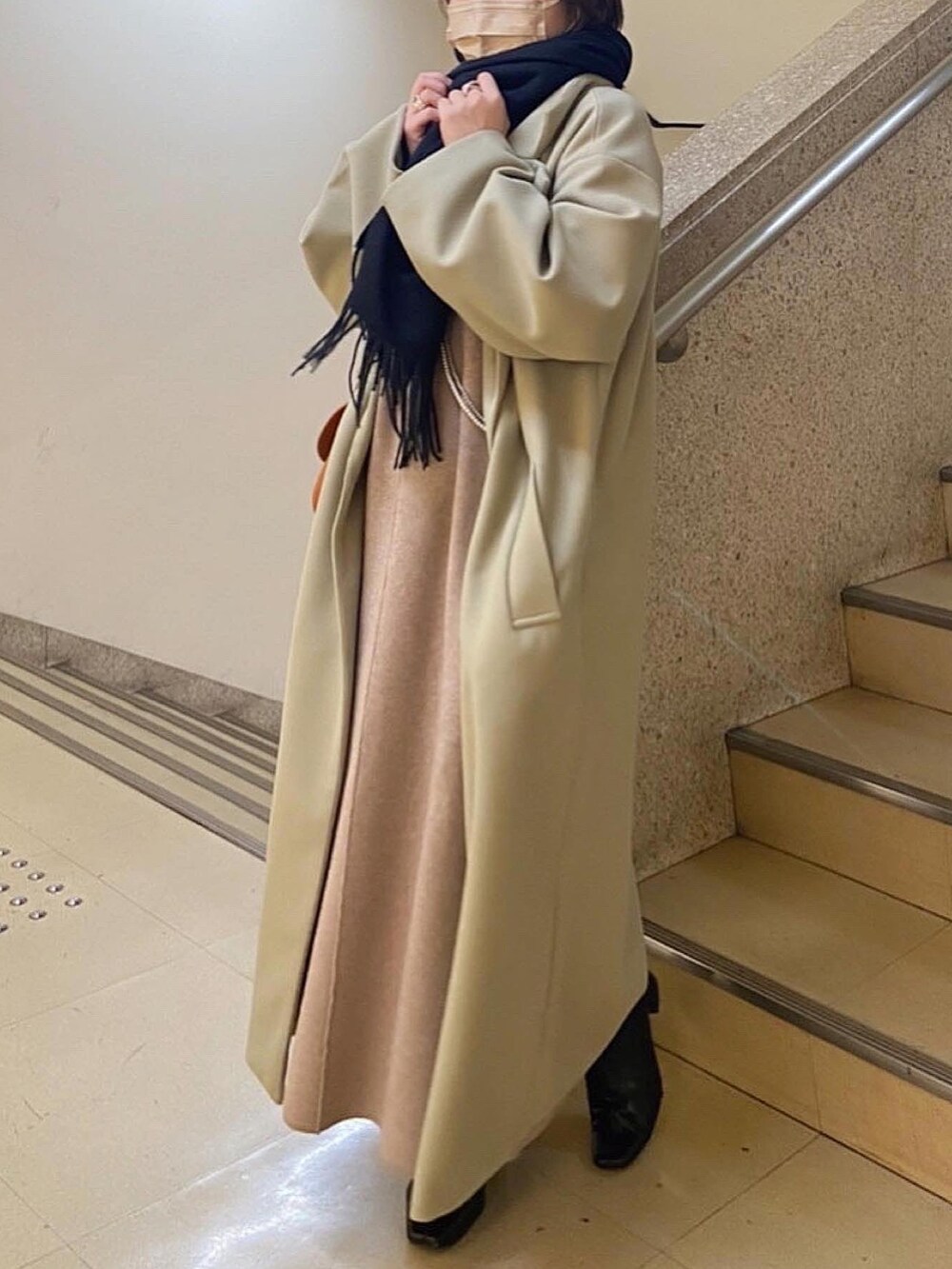 グリーン系のチェスターコート、ブラック系のショルダーバッグ、ベージュ系のワンピースを着用したレディースの冬コーディネートの2枚目の写真