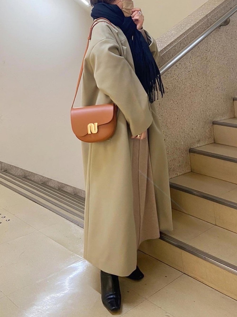 グリーン系のチェスターコート、ブラック系のショルダーバッグ、ベージュ系のワンピースを着用したレディースの冬コーディネートの3枚目の写真