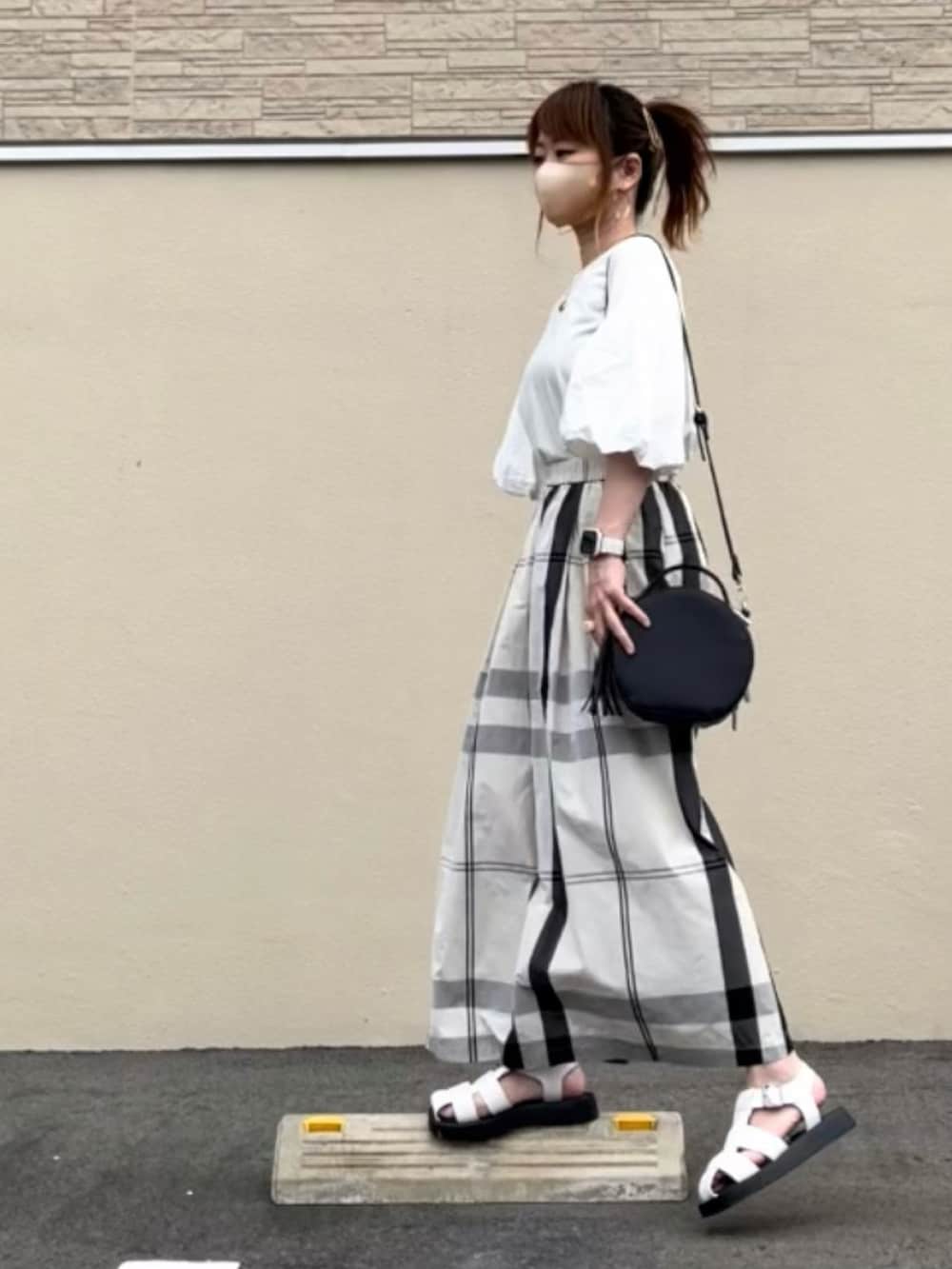 ホワイト系のスカート、ブラック系のトップス、ホワイト系のサンダルを着用したレディースの夏コーディネートの2枚目の写真