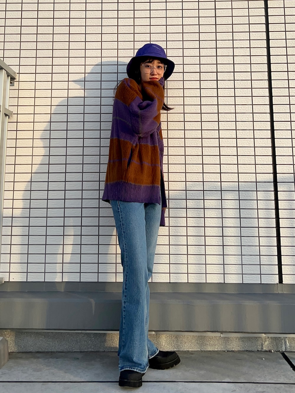 パープル系のカーディガン/ボレロ、ブルー系のデニムパンツ、ブラック系のブーツを着用したレディースの秋コーディネートの2枚目の写真