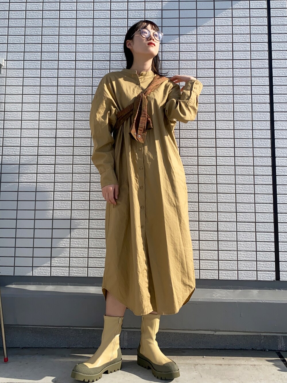 ベージュ系のシャツワンピース、グリーン系のブーツ、ブラック系のメガネを着用したレディースの春コーディネートの2枚目の写真