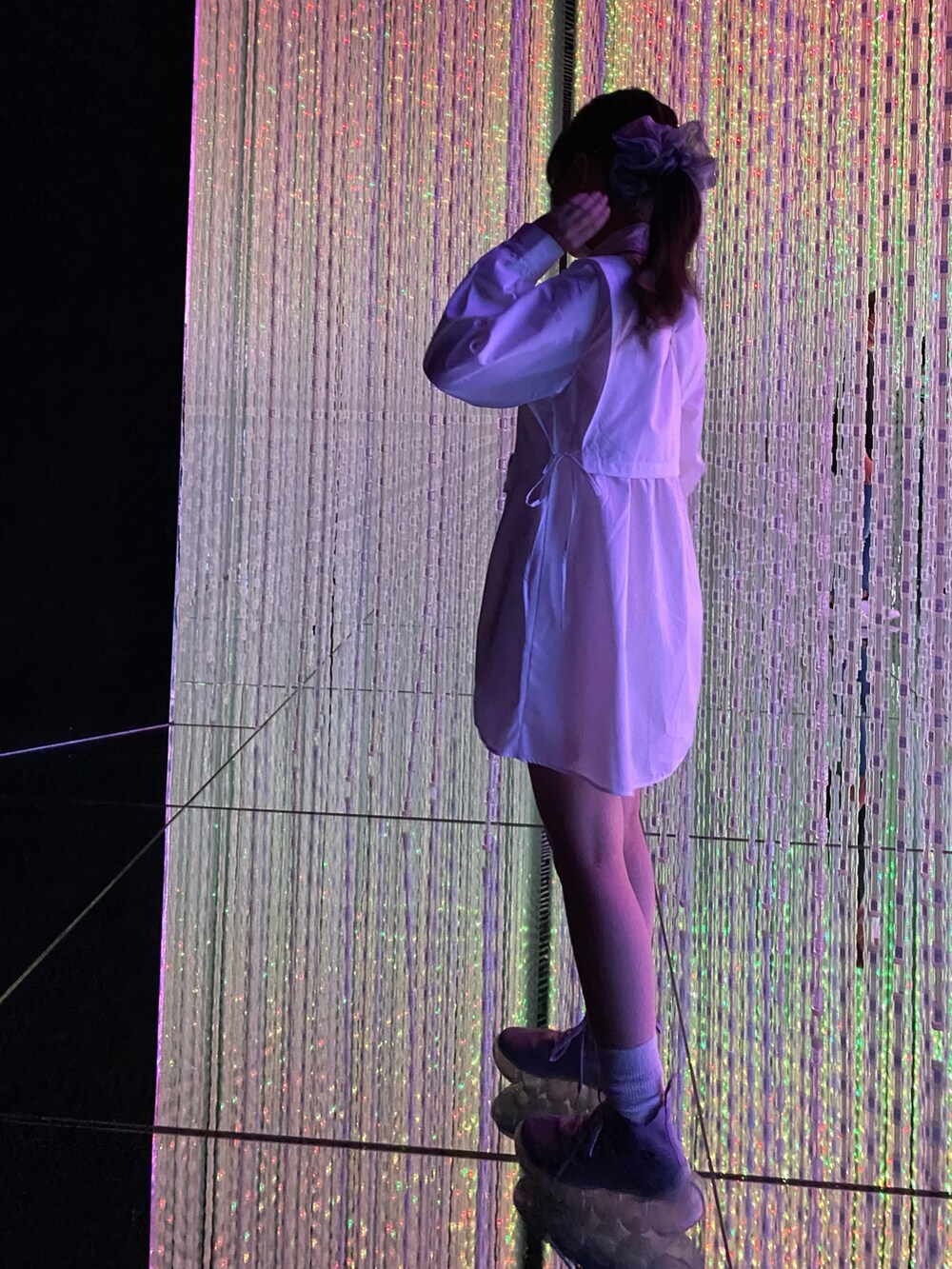 シルバー系のショルダーバッグ、ホワイト系のチュニック、パープル系のスニーカーを着用したレディースの夏コーディネートの2枚目の写真