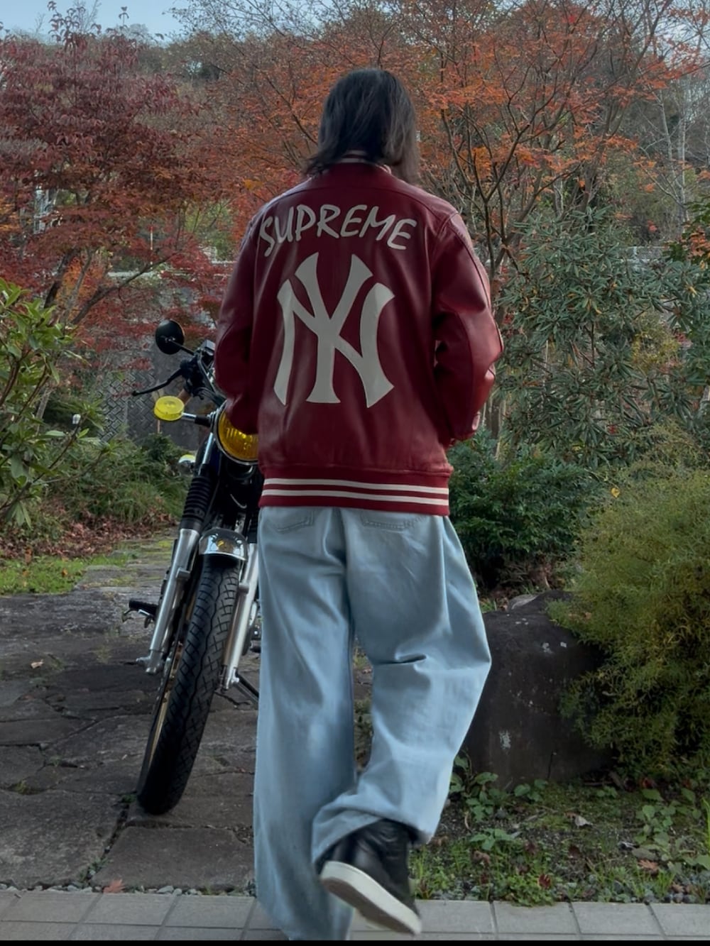 レッド系のスタジャン、ブルー系のデニムパンツ、ブラック系のスニーカーを着用したメンズの秋コーディネートの2枚目の写真