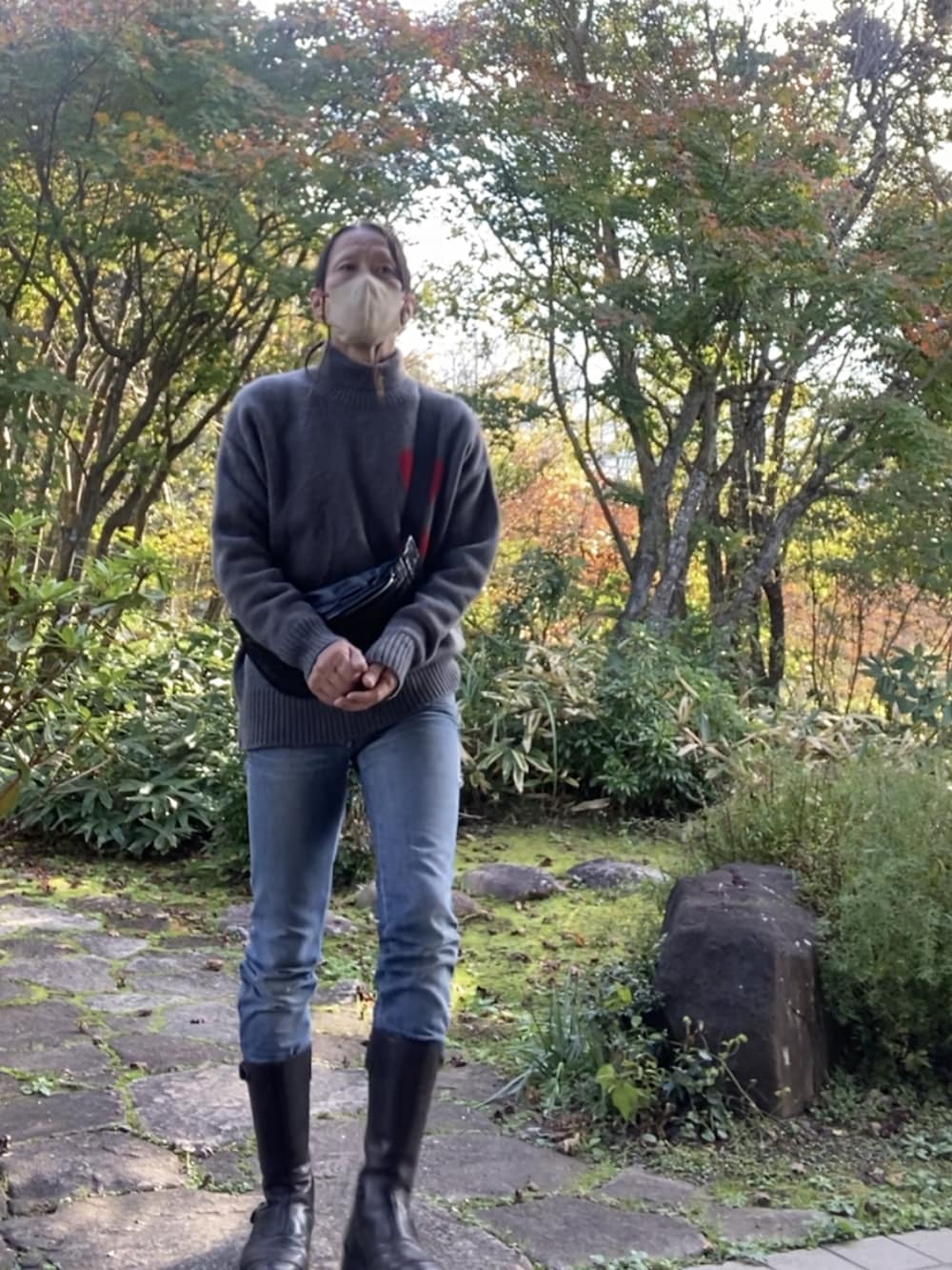 グレー系のニット/セーター、ブラック系のボディバッグ/ウエストポーチ、ブルー系のデニムパンツを着用したメンズの秋コーディネートの2枚目の写真