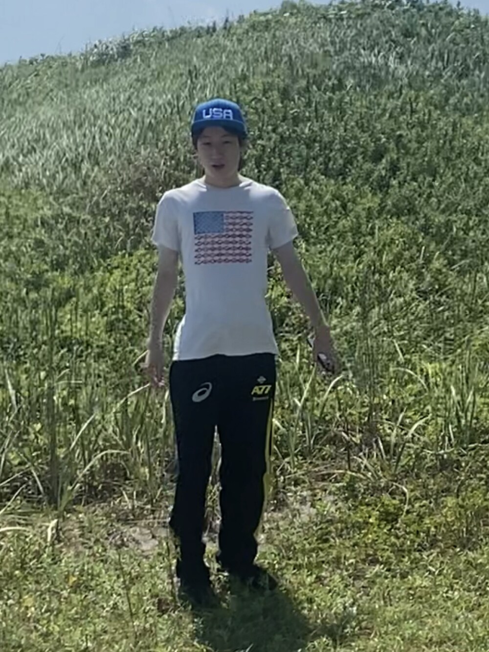 ベージュ系のTシャツ/カットソー、ブラック系のパンツ、ブラック系のスニーカーを着用したメンズの夏コーディネートの2枚目の写真