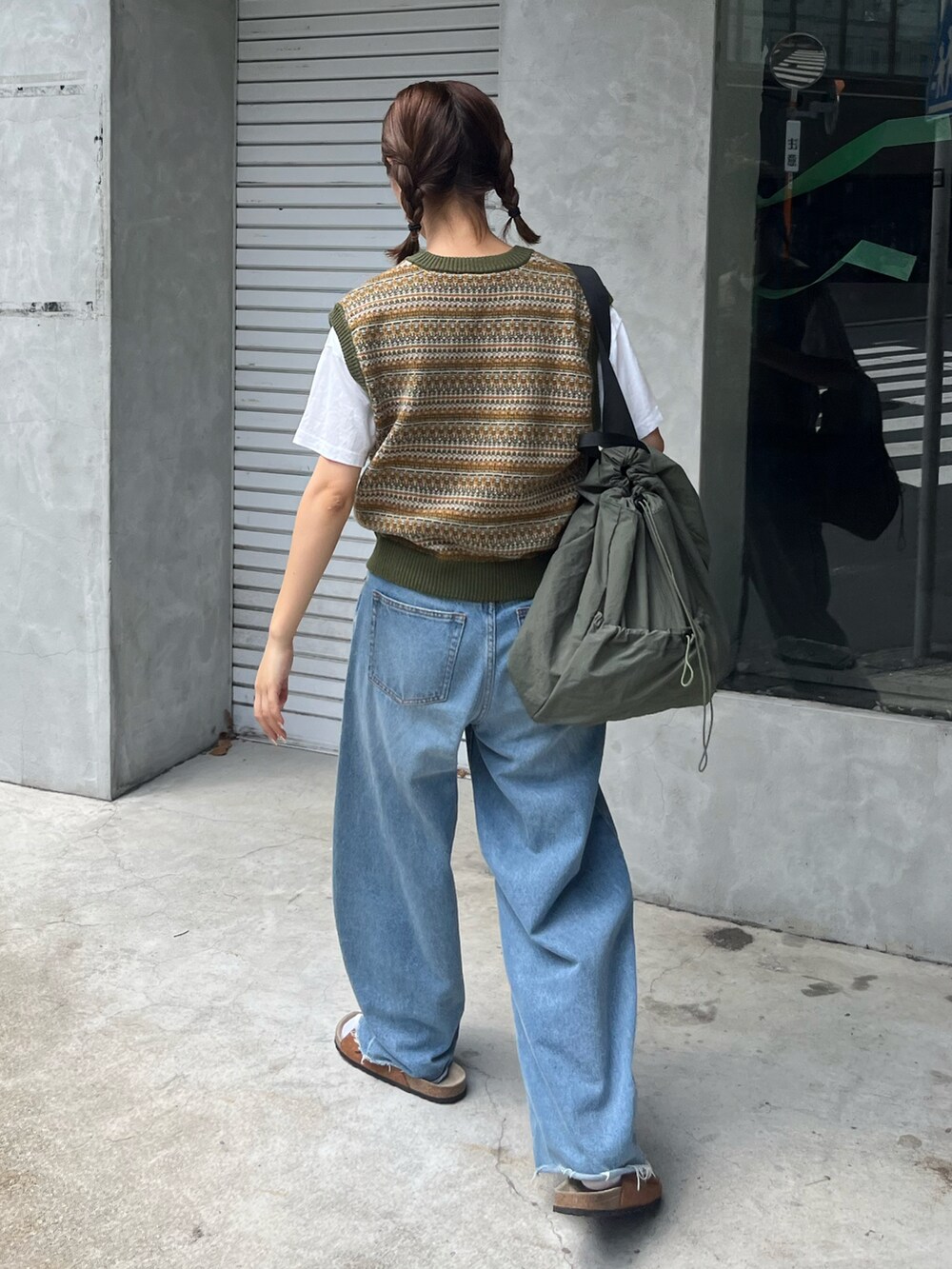 グリーン系のベスト、ブルー系のデニムパンツ、グリーン系のショルダーバッグを着用したレディースの秋コーディネートの2枚目の写真
