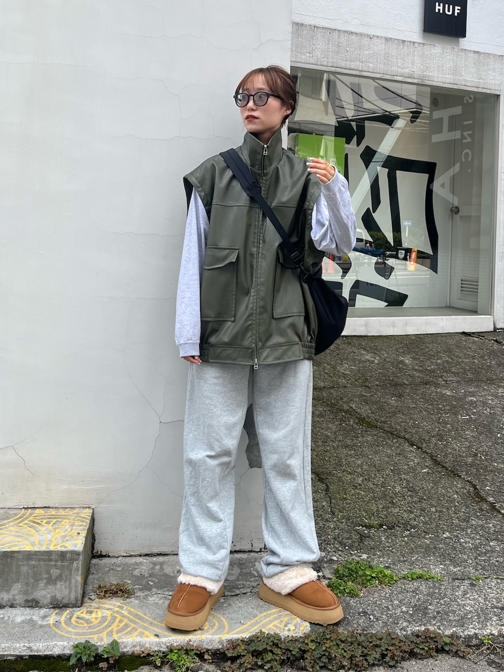 グリーン系のライダースジャケット、グレー系のスウェットパンツ、ブラウン系のサンダルを着用したレディースの秋コーディネートの2枚目の写真