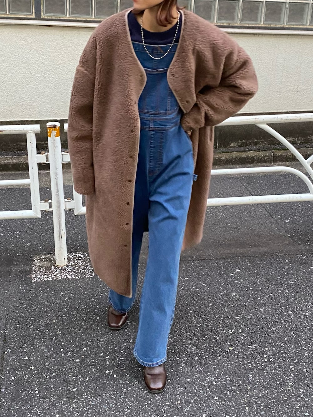 ブラウン系のノーカラーコート、ブルー系のサロペット/オーバーオール、ブラウン系のブーツを着用したレディースの秋コーディネートの2枚目の写真