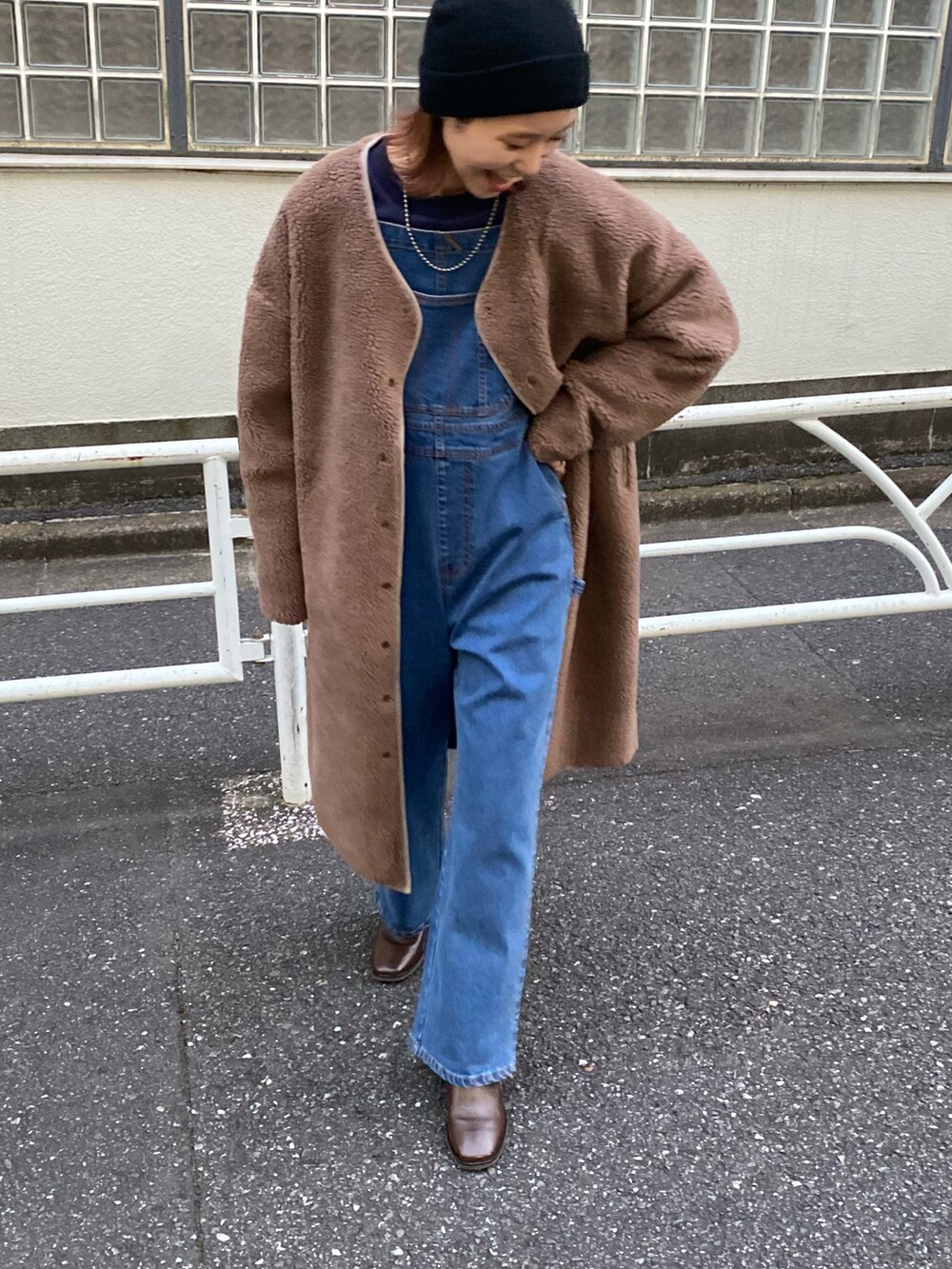 ブラウン系のノーカラーコート、ブルー系のサロペット/オーバーオール、ブラウン系のブーツを着用したレディースの秋コーディネートの3枚目の写真