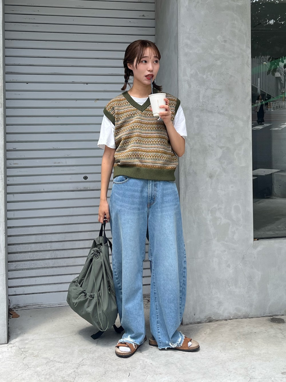 グリーン系のベスト、ブルー系のデニムパンツ、グリーン系のショルダーバッグを着用したレディースの秋コーディネートの3枚目の写真