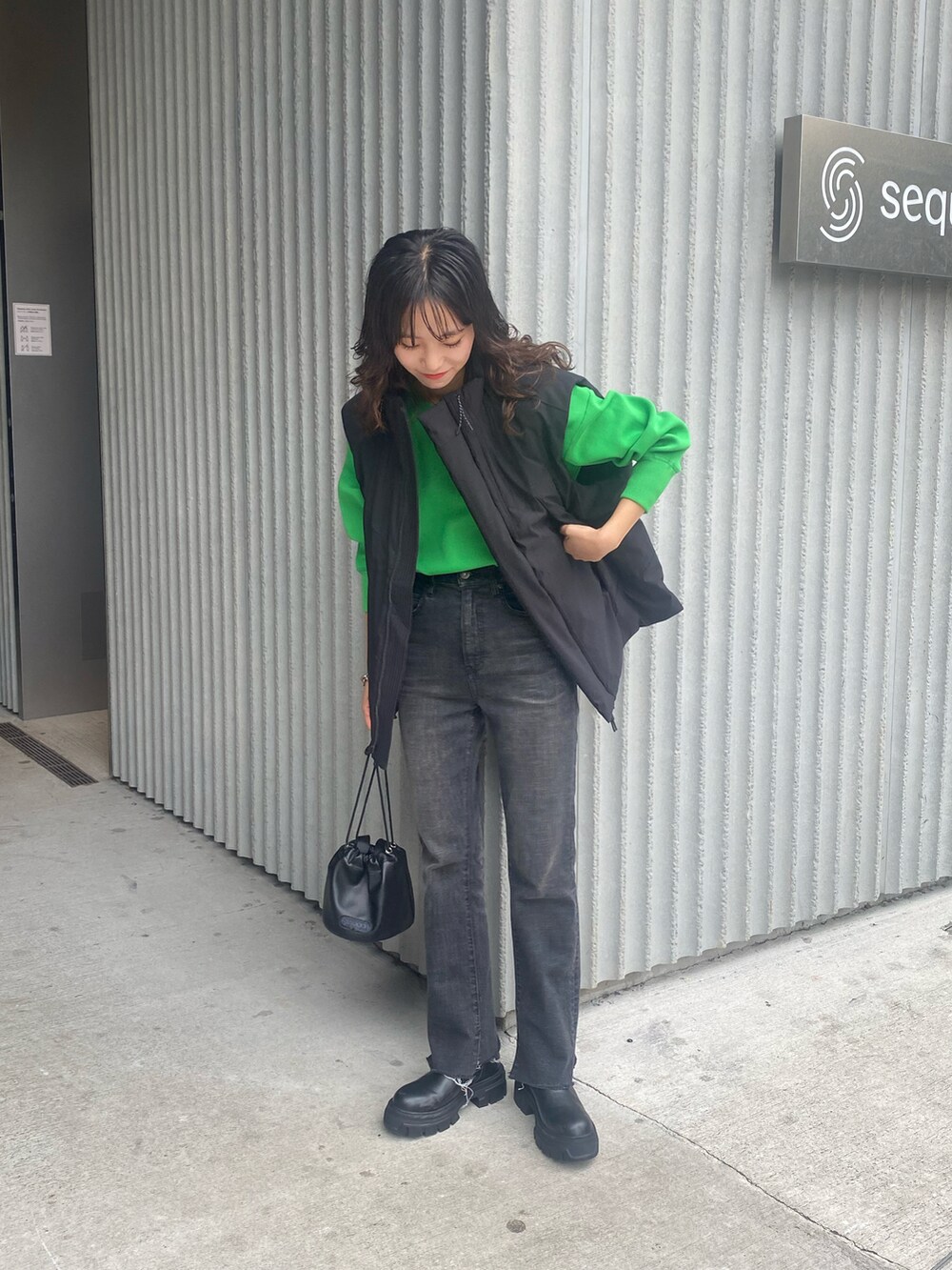 ブラック系のダウンベスト、グリーン系のニット/セーター、ブルー系のデニムパンツを着用したレディースの夏コーディネートの2枚目の写真