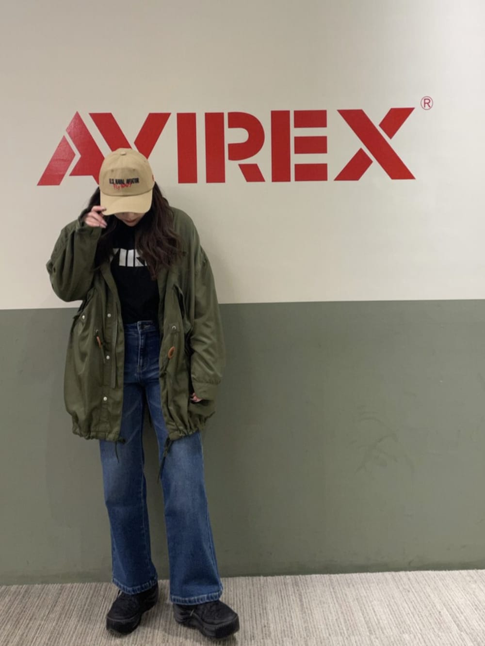 グリーン系のミリタリージャケット、ブルー系のデニムパンツ、ブラック系のニット/セーターを着用したレディースの春コーディネートの2枚目の写真