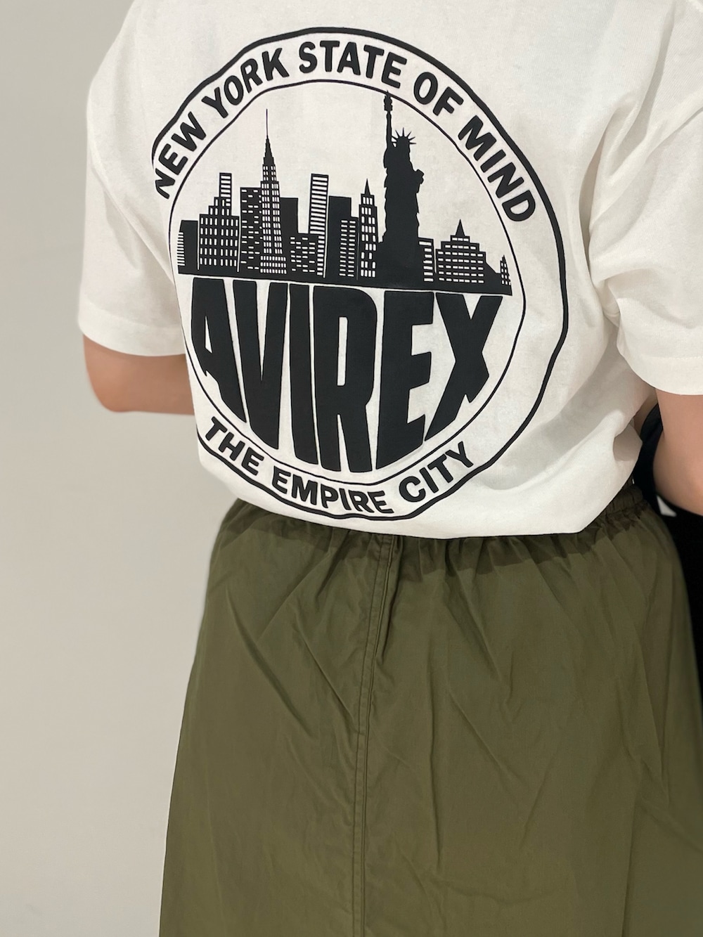 ブラック系のトートバッグ、グリーン系のスカート、ホワイト系のTシャツ/カットソーを着用したレディースの夏コーディネートの2枚目の写真