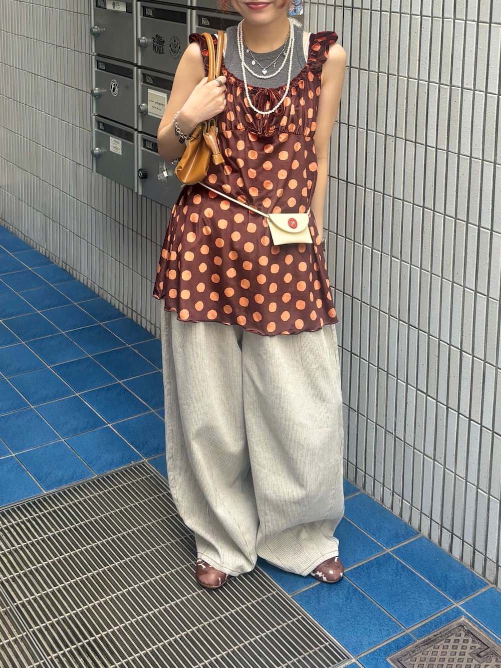 オレンジ系のチュニック、ホワイト系のボディバッグ/ウエストポーチ、ホワイト系のデニムパンツを着用したレディースの夏コーディネートの3枚目の写真