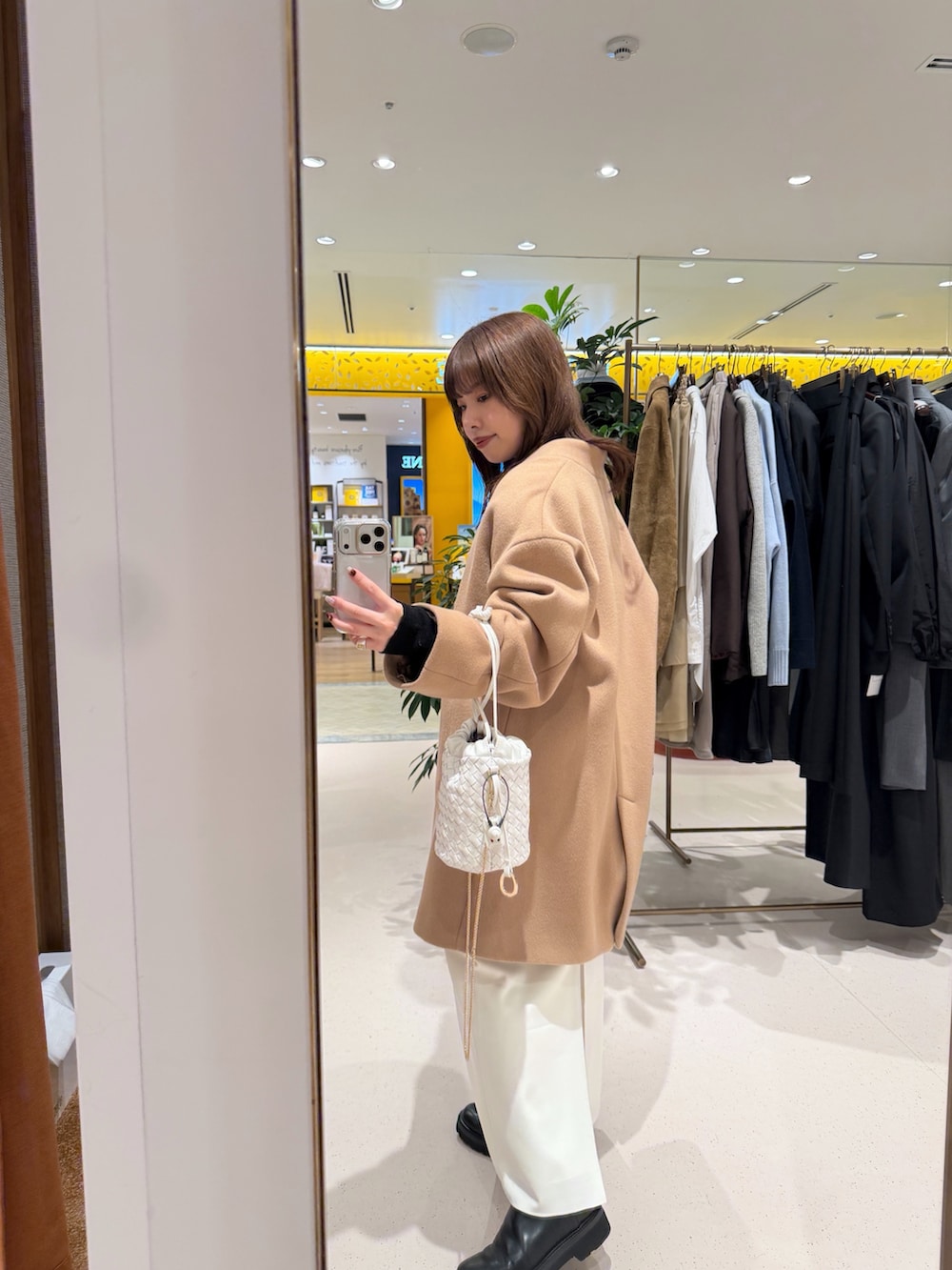 イエロー系のノーカラーコート、ホワイト系のショルダーバッグ、ブラック系のカーディガン/ボレロを着用したレディースの秋コーディネートの6枚目の写真