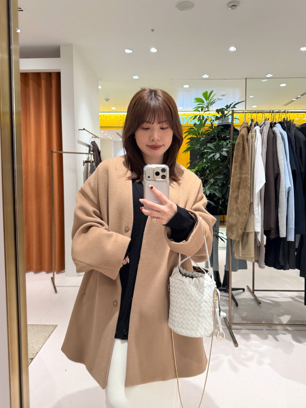 イエロー系のノーカラーコート、ホワイト系のショルダーバッグ、ブラック系のカーディガン/ボレロを着用したレディースの秋コーディネートの3枚目の写真