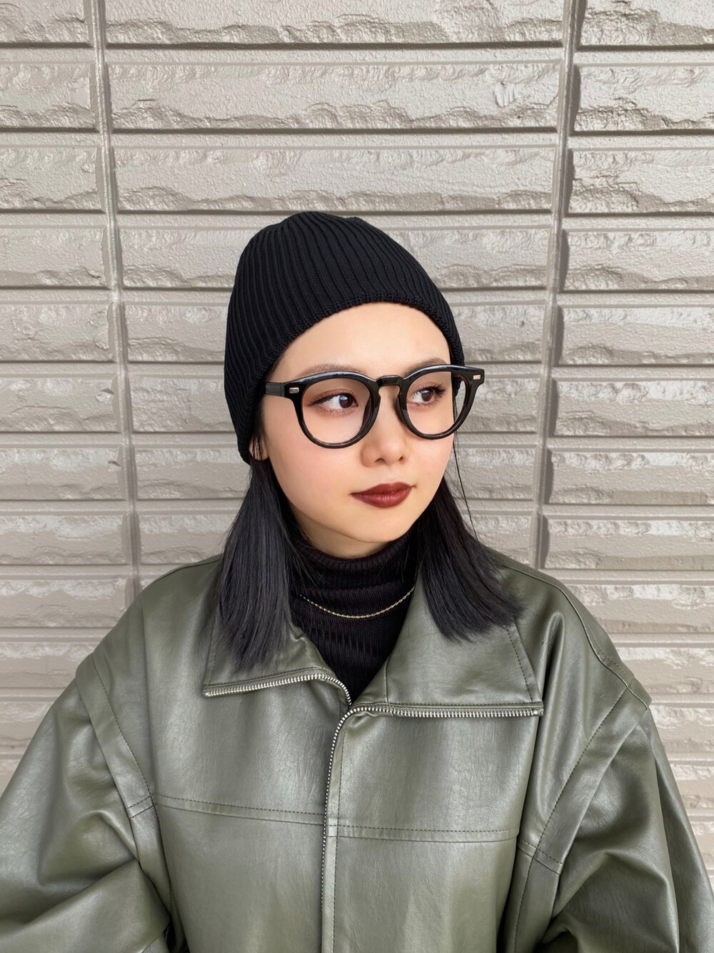 グリーン系のライダースジャケット、ブラック系のニット/セーター、ブラック系のハンドバッグを着用したレディースの春コーディネートの2枚目の写真