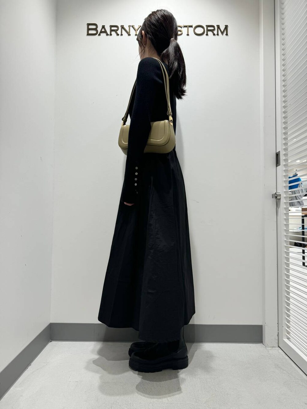 ブラック系のワンピース、ブラック系のブーツ、ベージュ系のショルダーバッグを着用したレディースの冬コーディネートの3枚目の写真