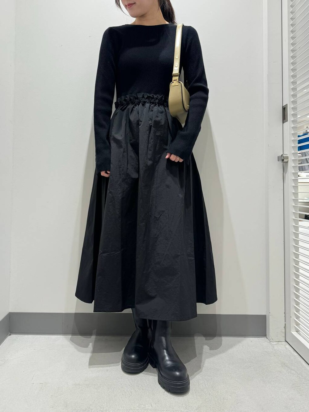 ブラック系のワンピース、ブラック系のブーツ、ベージュ系のショルダーバッグを着用したレディースの冬コーディネートの2枚目の写真