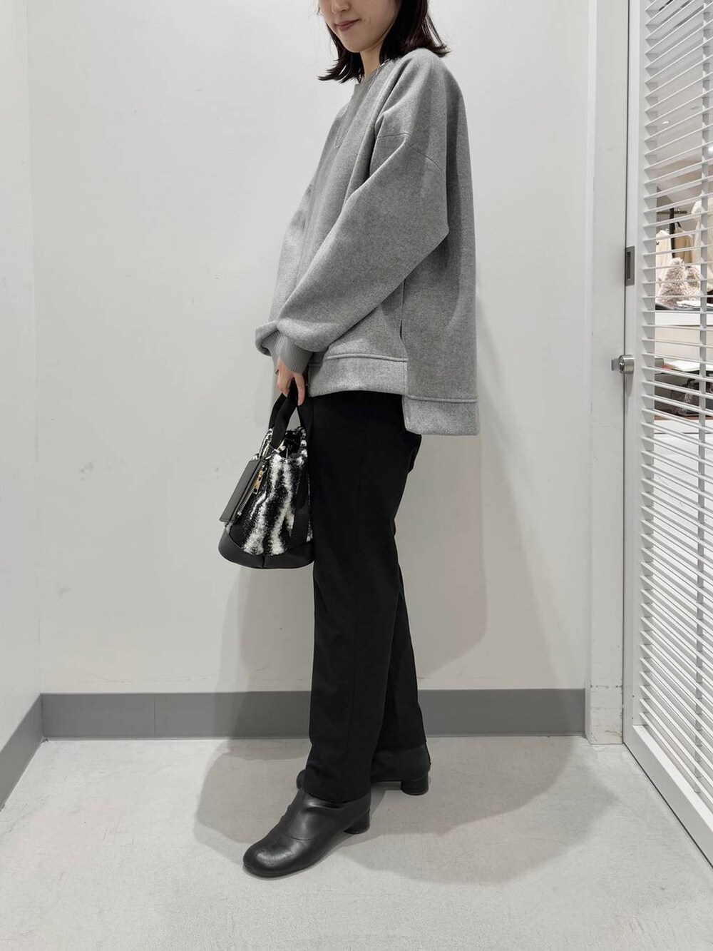 グレー系のパーカー、ホワイト系のトートバッグ、ブラック系のブーツを着用したレディースの冬コーディネートの2枚目の写真