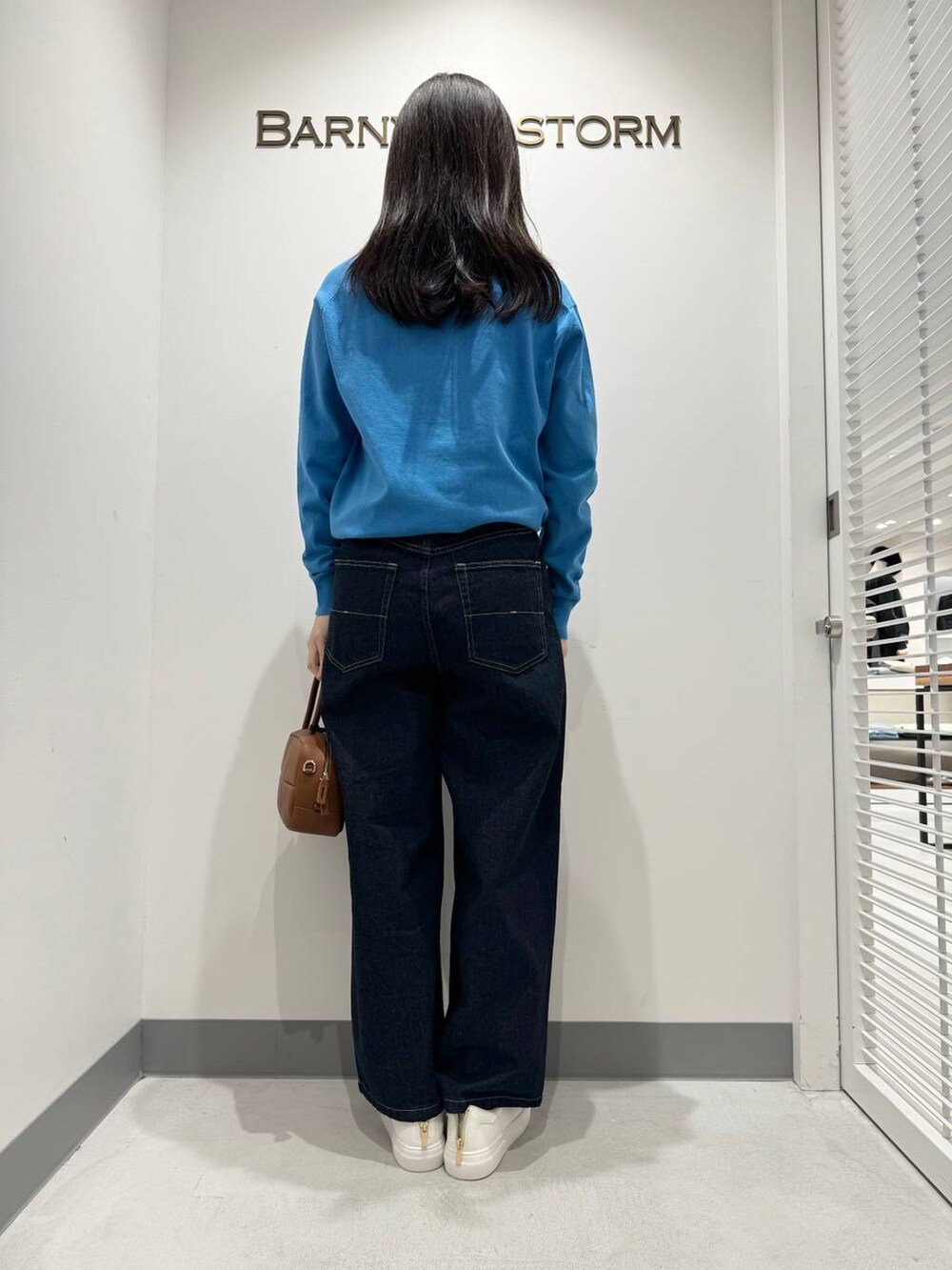 ブルー系のニット/セーター、ブルー系のデニムパンツ、ブラウン系のハンドバッグを着用したレディースの冬コーディネートの3枚目の写真